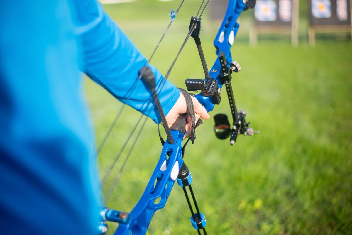 Archer aiming compound bow through sight pins at outdoor archery target