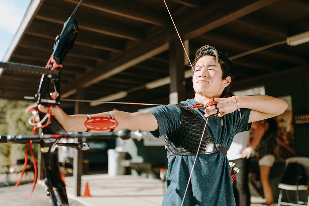 Archer aiming a recurve bow at an outdoor archery range demonstrating proper arrow spine alignment