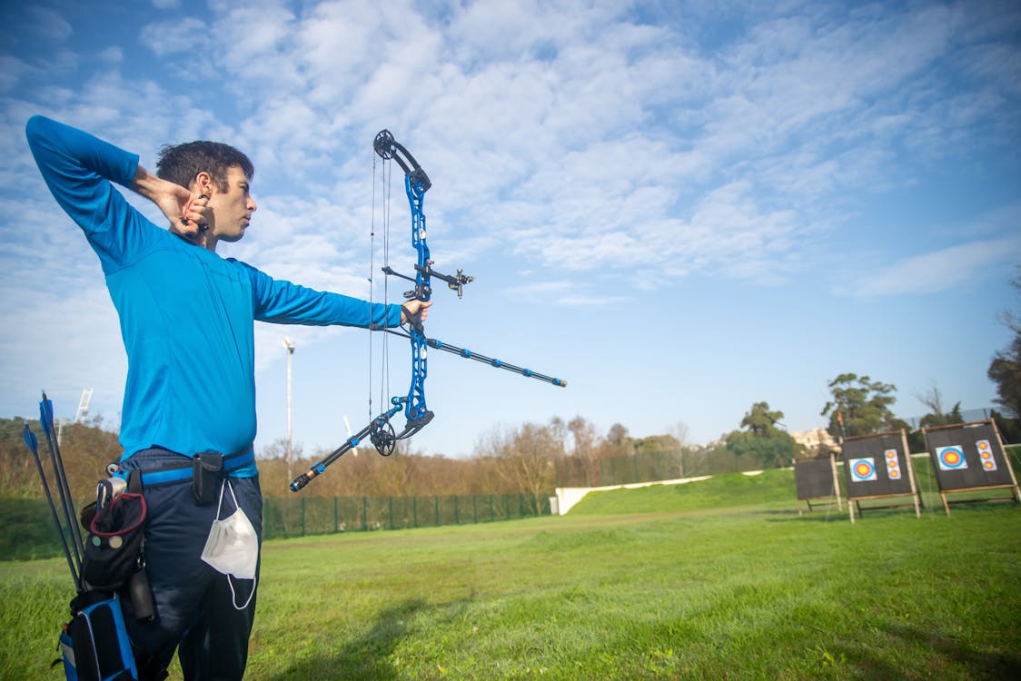 Archer aiming compound bow outdoors representing LA28 Olympic archery qualification
