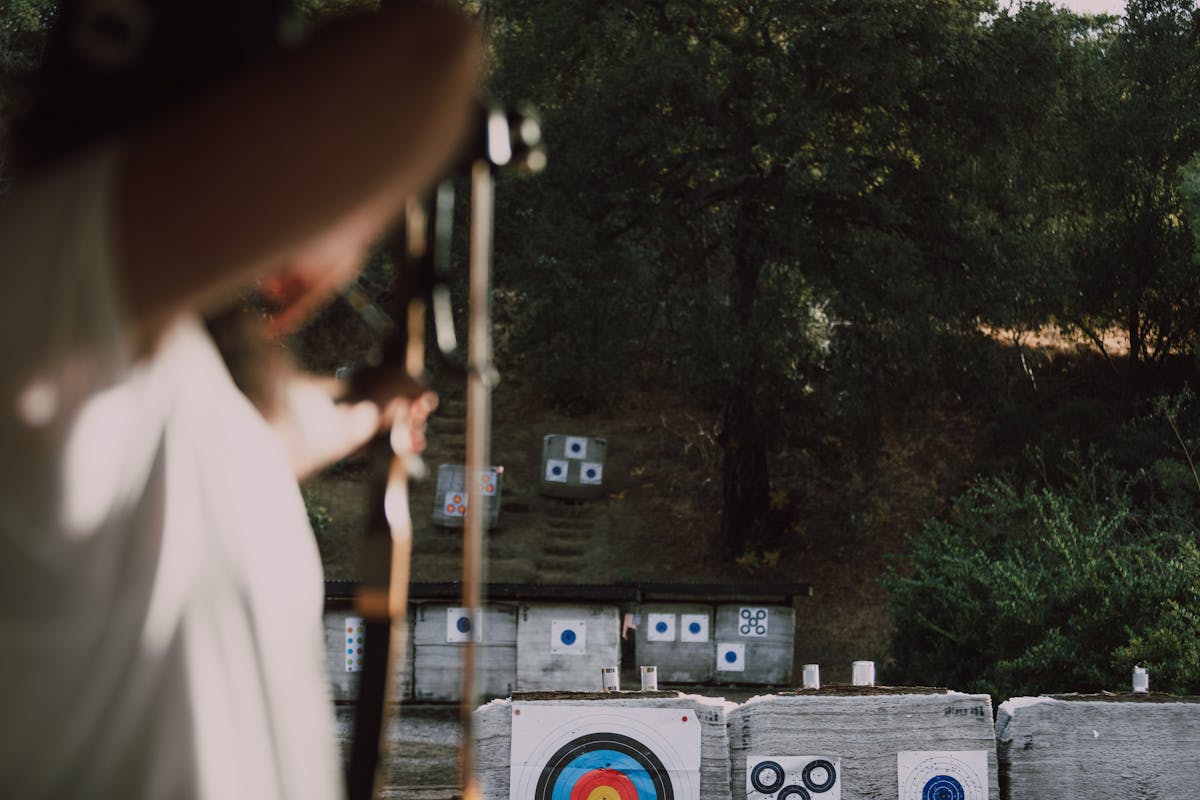Focused archer aiming through trees with stabilizer bar visible on the bow