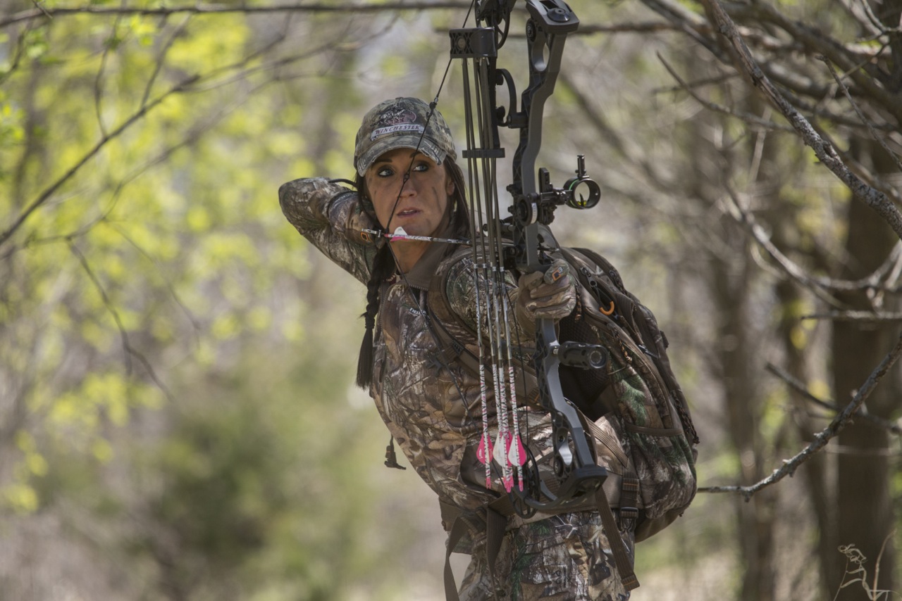 Bowhunter in camouflage aiming compound bow during spot and stalk