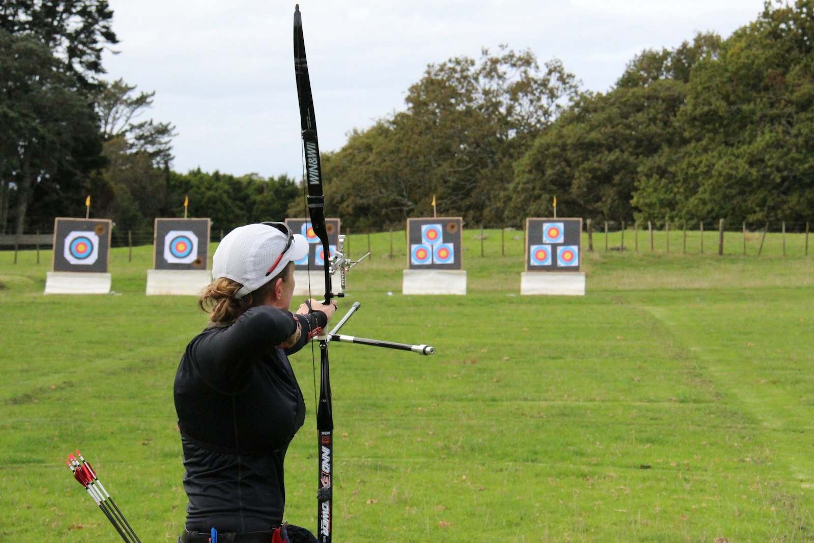 Female recurve archer shooting at multiple outdoor target faces on grass field