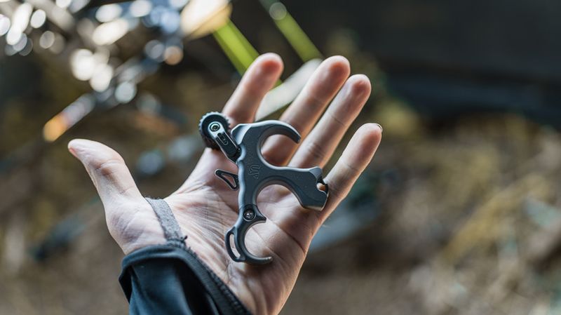 Archery button release handheld grip in shooter palm with bow gear in background