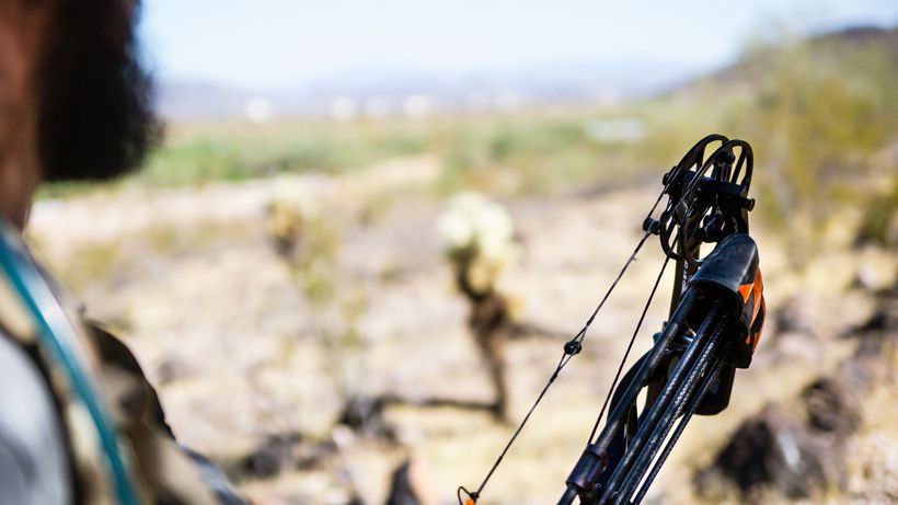 Bowhunter at full draw with compound bow in Western terrain