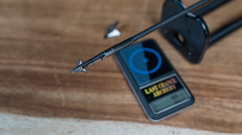 Weighing a broadhead-tipped arrow on a grain scale before broadhead tuning