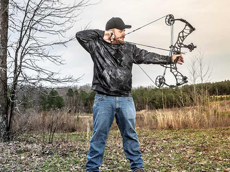 Archer aiming a compound bow at full draw in a field