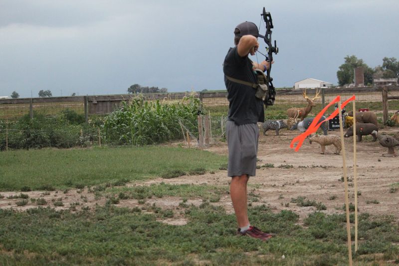 Archer shooting a compound bow at distant targets with a wind flag
