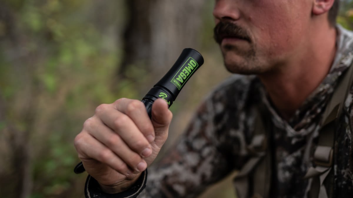 Bowhunter holding a deer grunt call tube in fall woods
