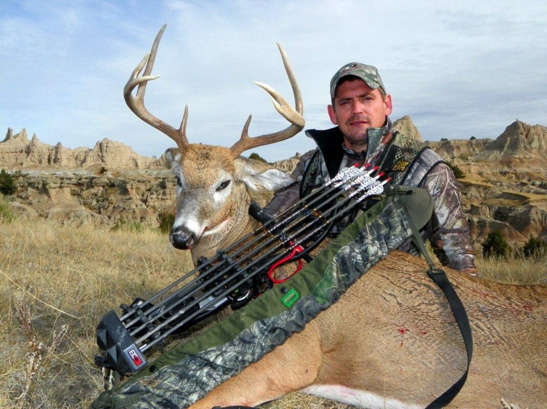 Bowhunter with whitetail buck and compound bow showing fletched hunting arrows