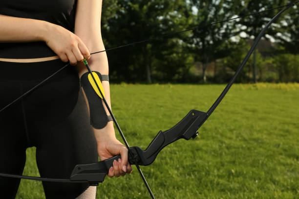 Woman with bow and arrow practicing archery in park, closeup Woman with bow and arrow practicing archery in park, closeup rec