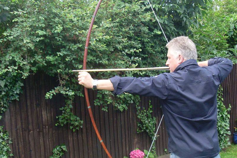 Archer at full draw shooting an English-style longbow in a backyard, illustrating the recurve vs longbow draw cycle