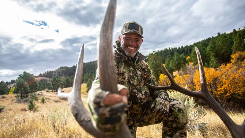 Spot and stalk bowhunter with mule deer in western terrain