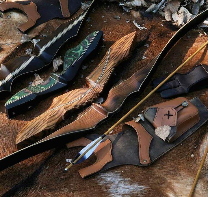 Traditional recurve bows laid out with a leather quiver, arm guard, and arrows