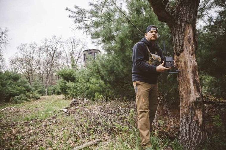 Bowhunter setting up trail camera at a pinch point for summer scouting