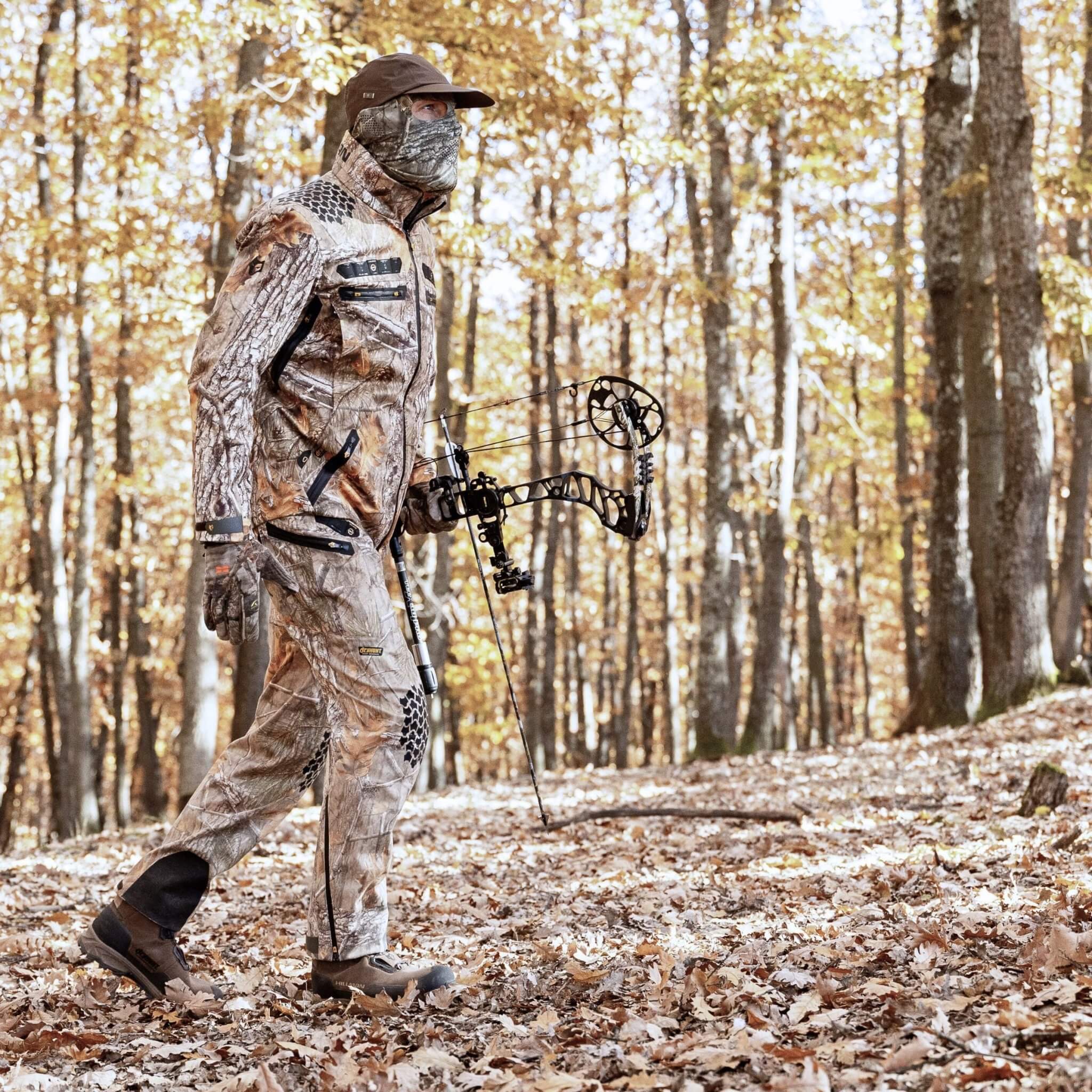 Wearing Hillman’s Cold Weather Camo Pants - Winter Hunting AlphaShell | 6OL, a hunter walks through a sunlit autumn forest wi