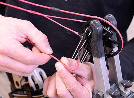 Archer twisting a bow cable to adjust and fix cam timing on a compound bow