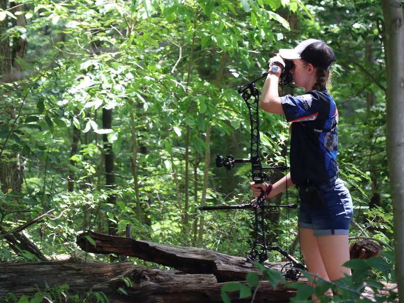 Young archer aiming a compound bow on a wooded 3D archery course