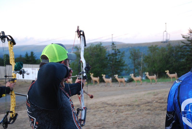 Compound archer aiming at 3D archery foam animal targets on a mountain course