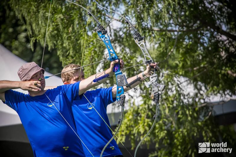 Two recurve archers drawing bows side by side on the range