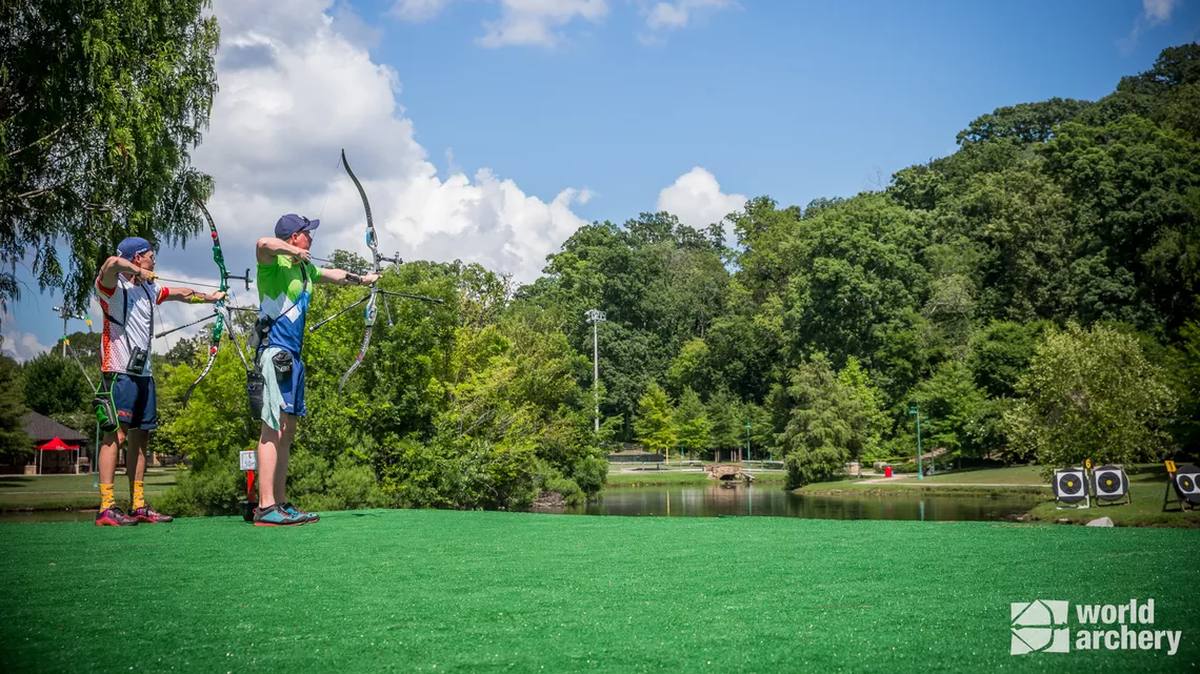 Two archers aiming recurve bows on an outdoor archery range
