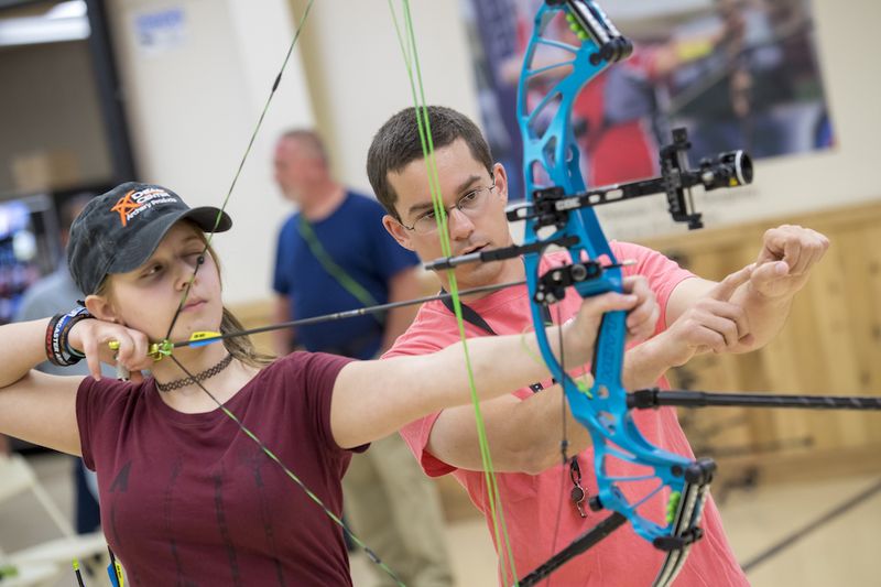 Coach adjusting an archer's stance and body alignment while shooting