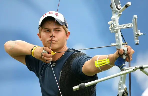Archer aiming a recurve bow while practicing at a backyard archery range