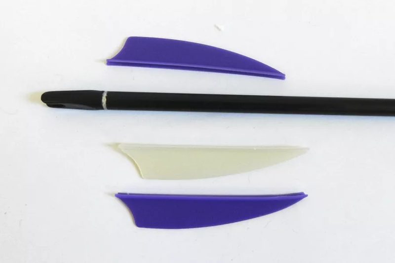 Bare arrow shaft with loose plastic vanes before fletching an arrow