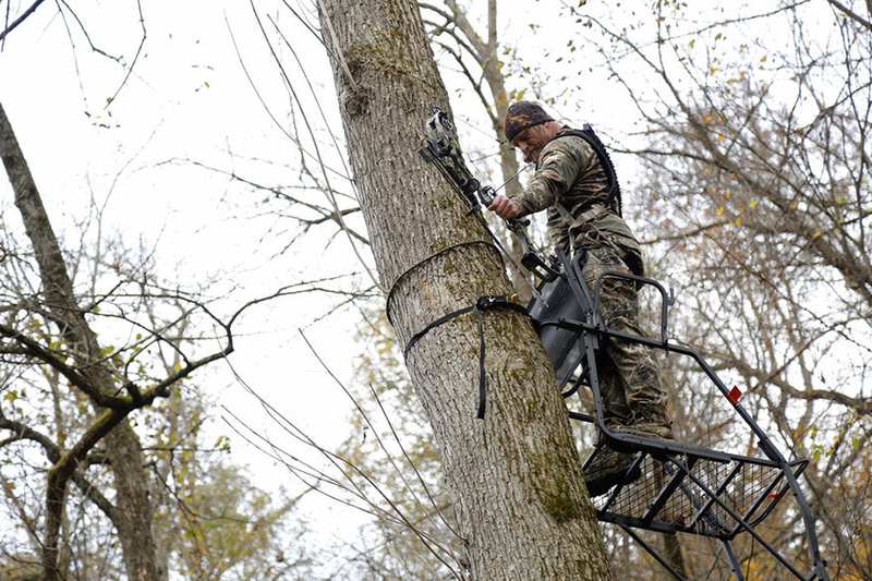 Bowhunter hanging and setting up tree stand on oak tree