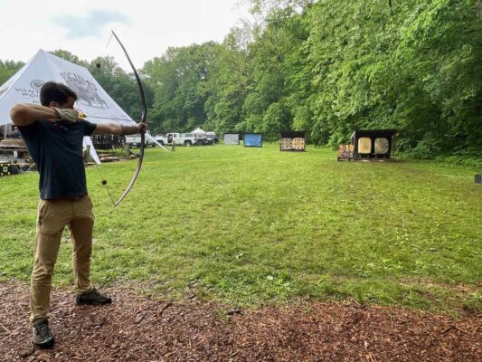 Archer at full draw with a braced recurve bow at an outdoor range