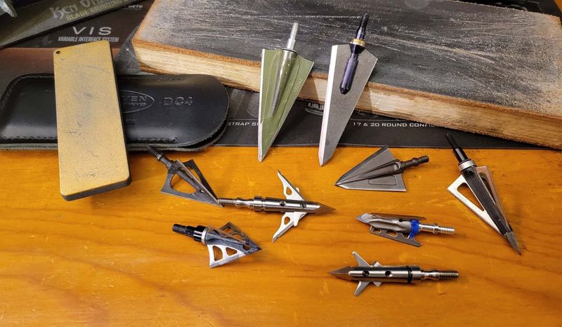 Sharpening a broadhead blade with a flat file and stones on a bench