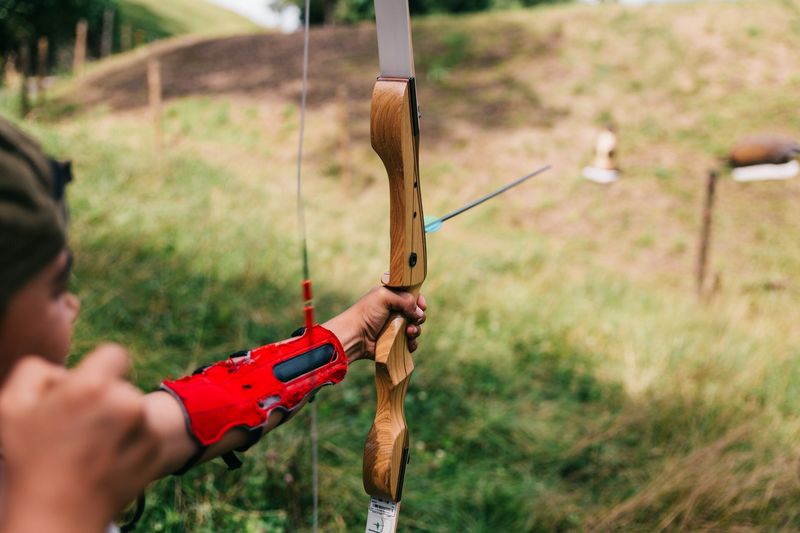 Recurve archer wearing red arm guard while shooting at outdoor archery range